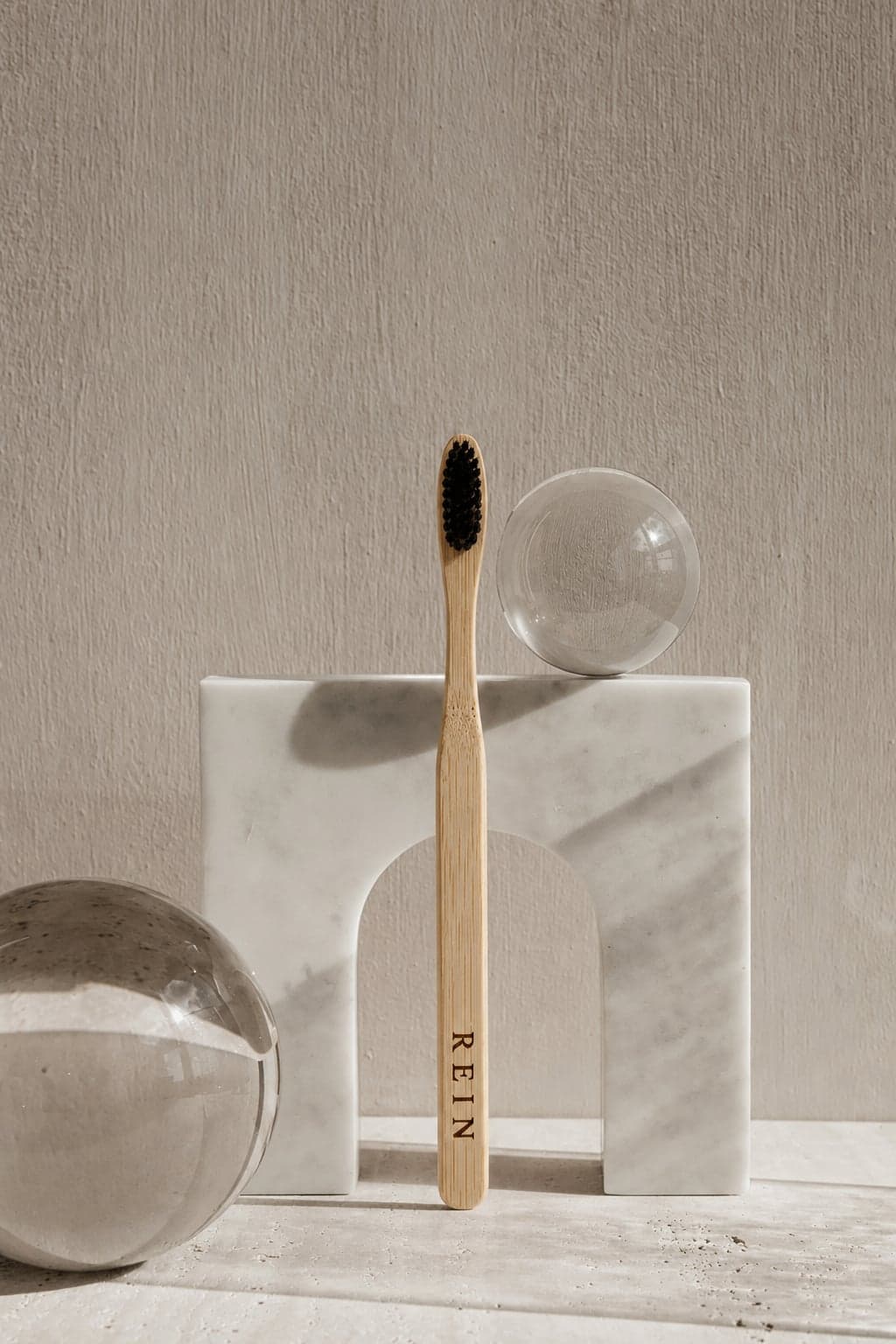 Toothbrush No. 01 — bamboo handle and dark bristles, standing against a marble arch